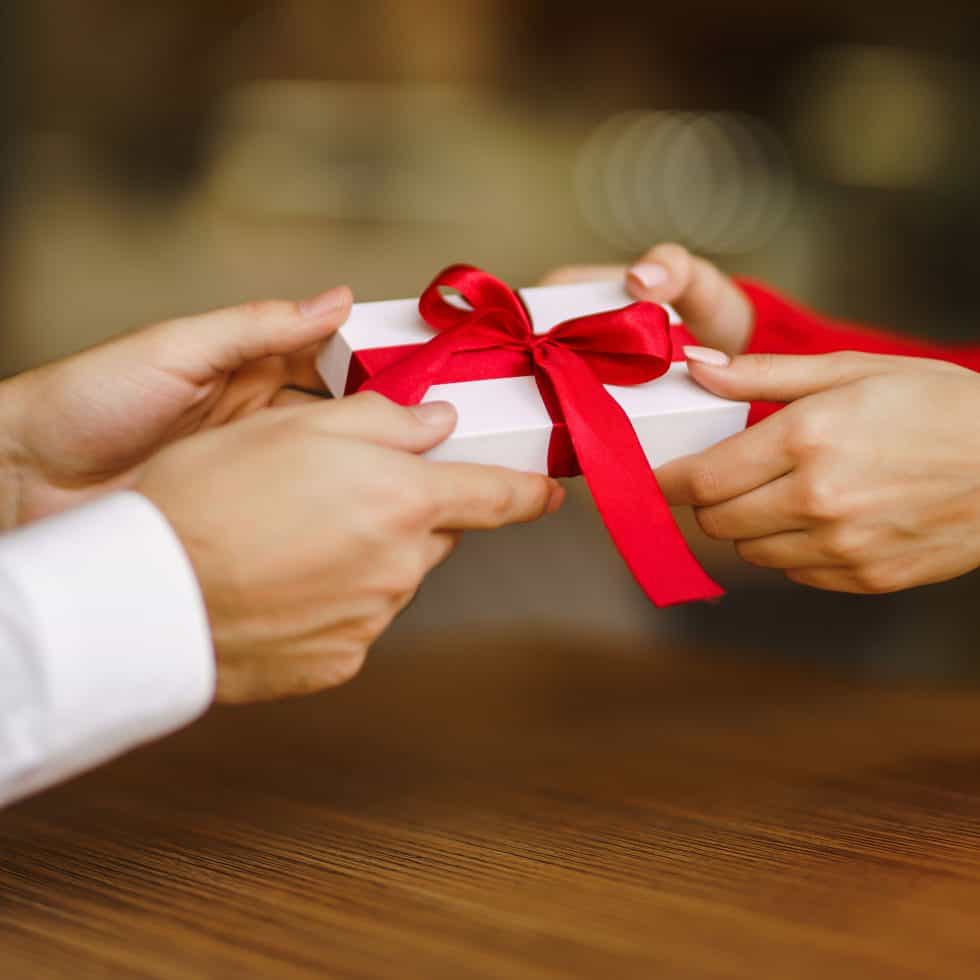 white gift box with red ribbon being given as a gift from the gift shop