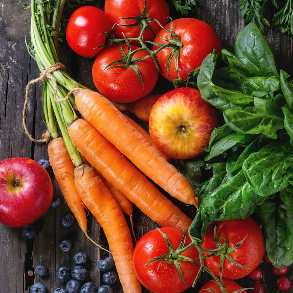 Fresh, bright vegetables including carrots and spinach with veggies like blueberries, tomatos and carrots on a rough wood background for Produce Department